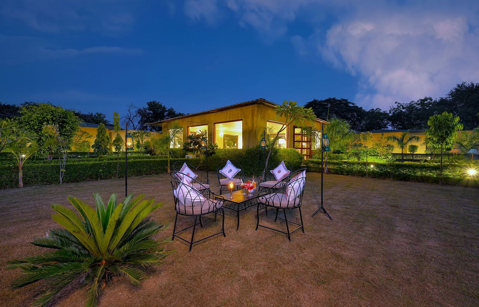 A serene garden at night featuring a table and chairs surrounded by lush greenery and soft lighting - Singhvilas, Ranthambore