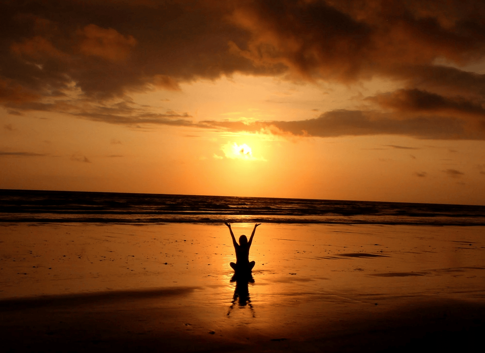 View of a woman from the back facing a beach with sunset in the background.