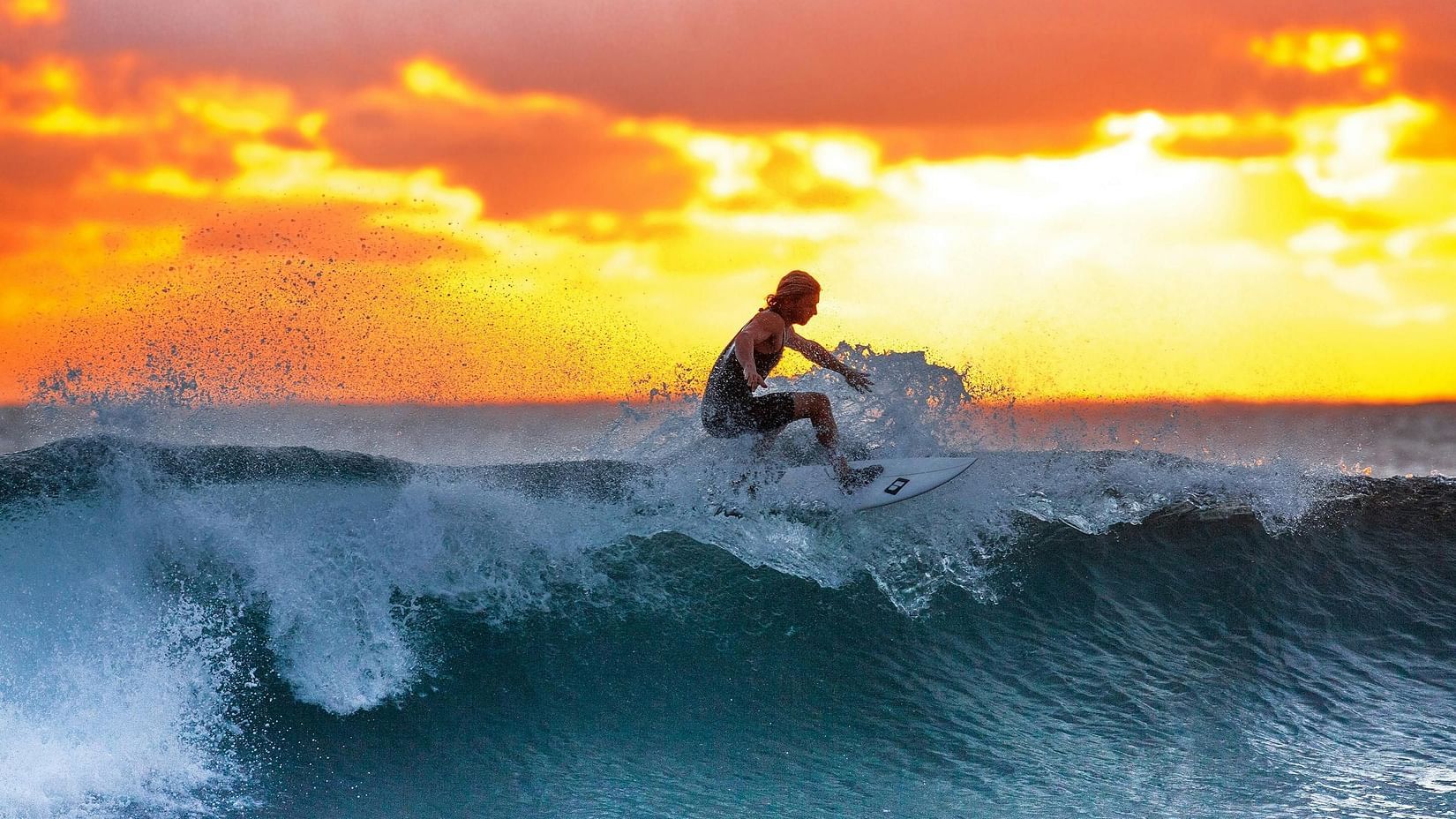 image of a person surfing through the waves with a bright sunset at the background