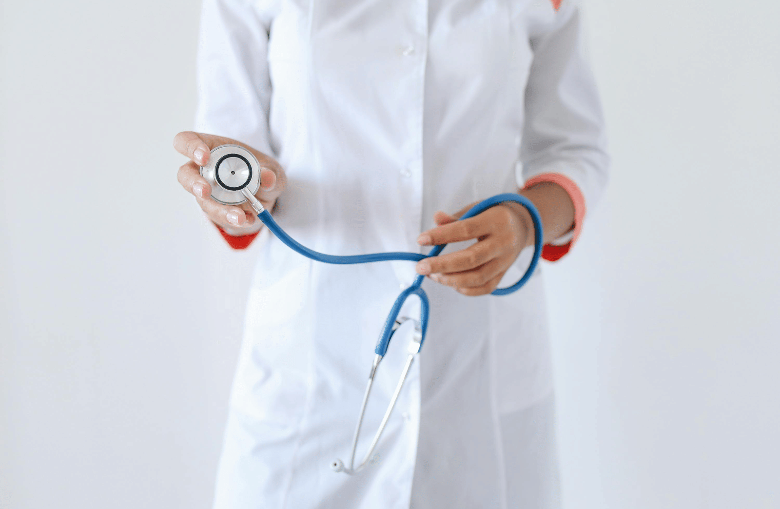 A close-up view of a person in a white medical coat holding a blue stethoscope with both hands.