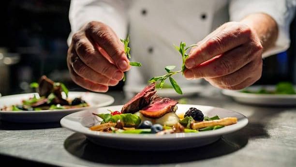 A chef meticulously garnishing a plate of food with fresh herbs in a professional kitchen setting.