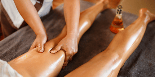 A pair of hands massaging the lower thigh of a person lying on their stomach