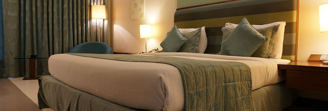 A double bed with pillows and cushions kept neatly against the head board of the bed in a warmly lit room.
