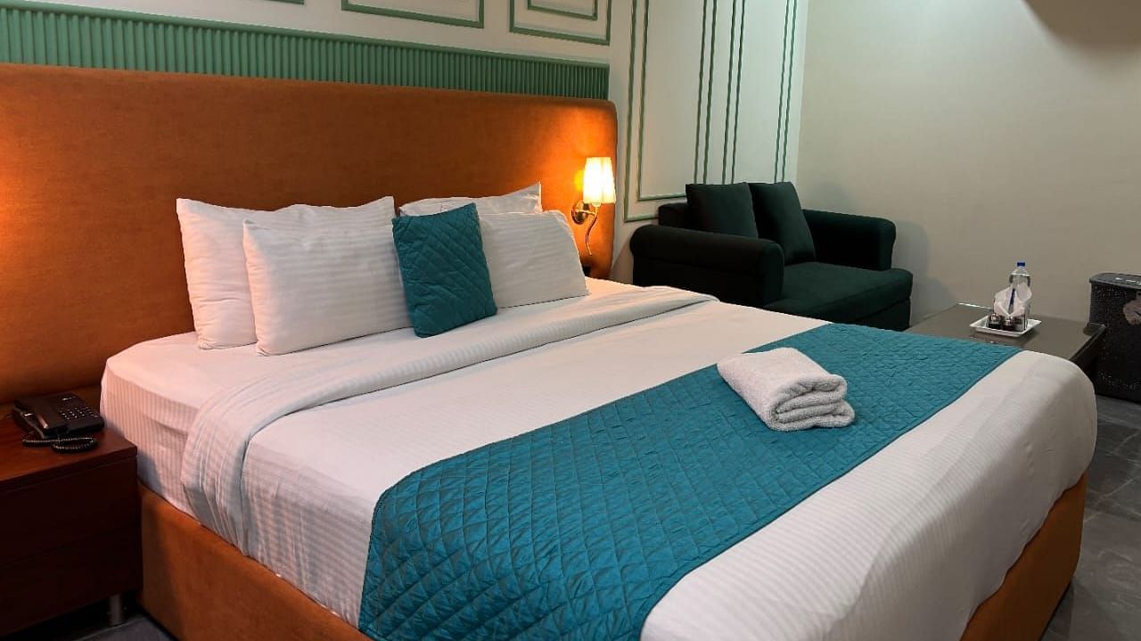An interior view of a hotel room featuring a bed with pillows,  a sofa and decorative wall paneling - Asian Suites IFFCO Chowk Metro Station, Gurgaon. 