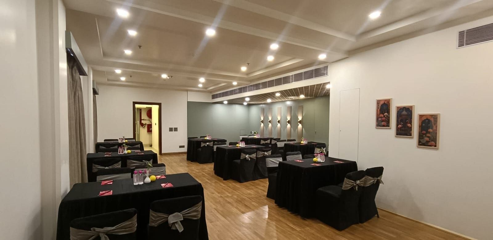 Conference room with rectangular tables covered with black satin covers and chairs under white ceiling lights at Lords Plaza Jaipur.