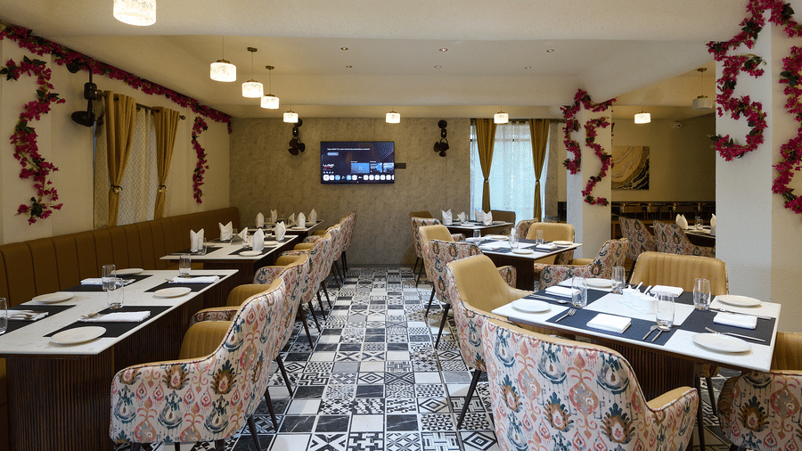 An indoor restaurant dining area with multiple set tables, patterned chairs, a TV screen, and floral garland decorations | Voyage Eastin Suites