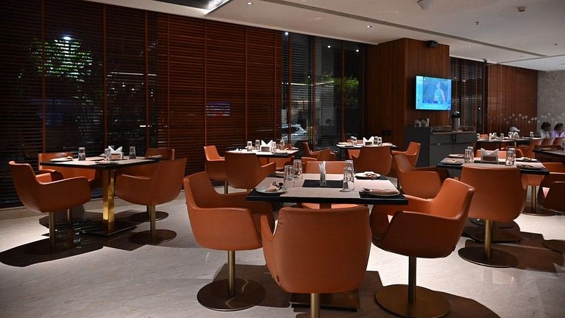 A contemporary dining area with round tables and orange chairs set against a warm, wooden backdrop.