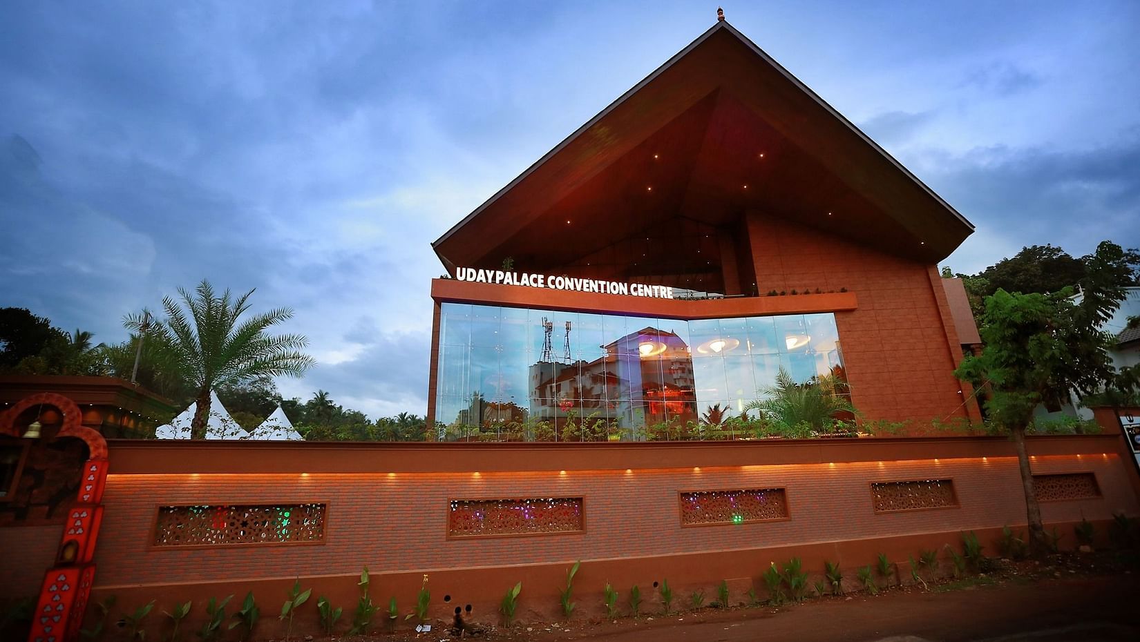 Facade of well-lit Uday Palace Convention Centre under a cloudy blue sky