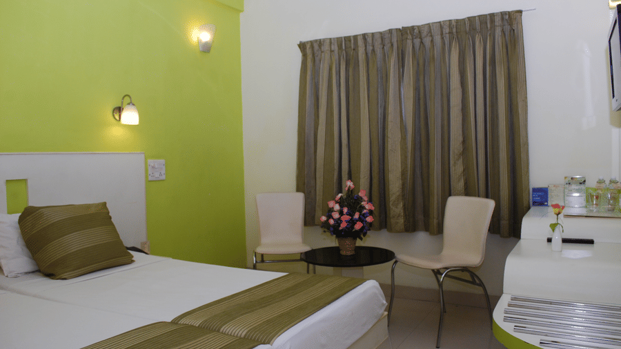Hotel bedroom interior with adjoined twin beds, a light green accent wall, and a small coffee table seating arrangement - Hotel Pandian