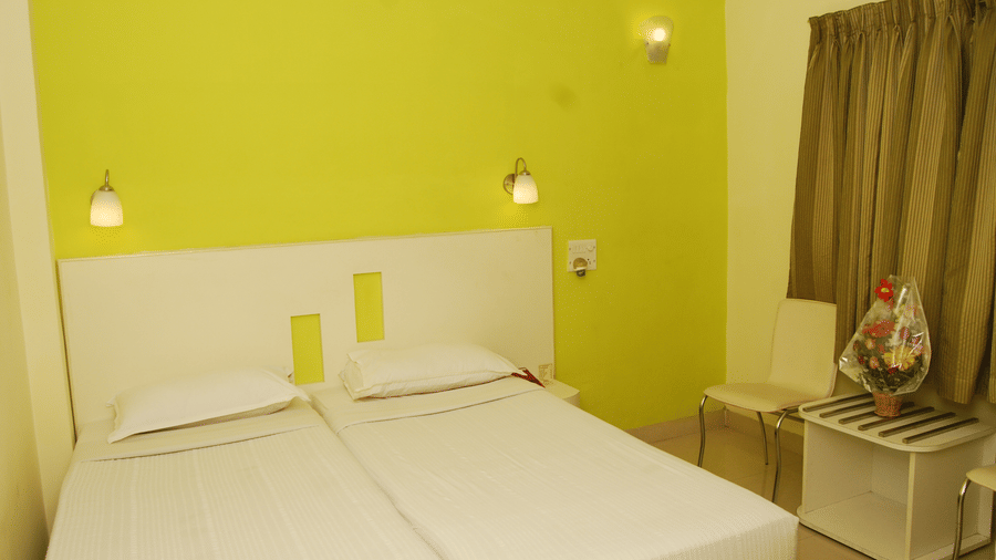 Hotel accommodation showing 2 beds made with white linens against a vibrant yellow wall near a window with curtains - Hotel Pandian