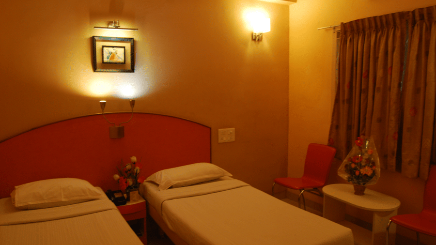A budget hotel twin room showing 2 single beds with a distinctive red-orange wooden headboard and warm ambient lighting - Hotel Pandian