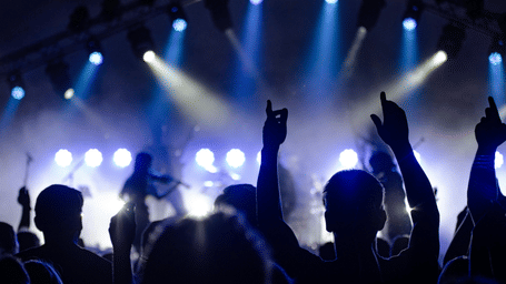 A live music performance with an audience raising hands under stage lights