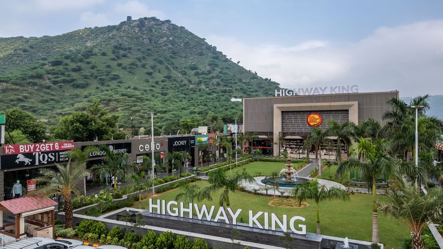 Diagonal exterior view of Hotel Highway King, Neelka, set against a cloudy sky with lush mountains in the background.