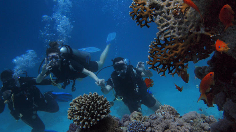 3 divers posing near a coral reef underwater, enjoying one of the water sports activities in Neil Island.