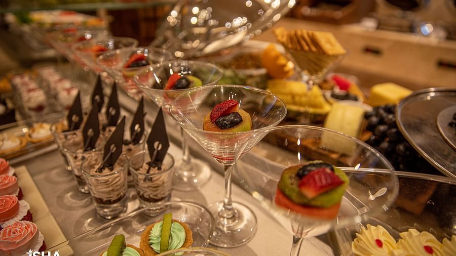 A close-up view of a dessert buffet with various small, elegantly arranged treats in glasses and on plates. Fresh fruit, chocolate decorations, and other garnishes are visible.