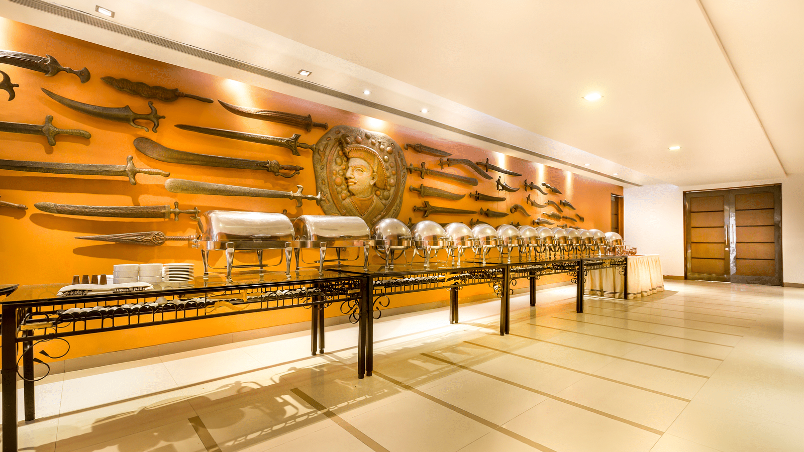 Hotel   with a long buffet table, ornate wall decor featuring swords and shields, and warm lighting.