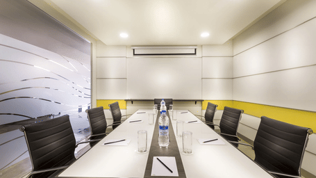 A conference room at Regency Tiruttani by GRT Hotels with long table, chairs, display screen, and ceiling lighting.