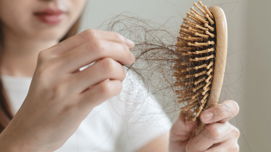 A woman holding a wooden hairbrush while pulling out loose strands of hair.