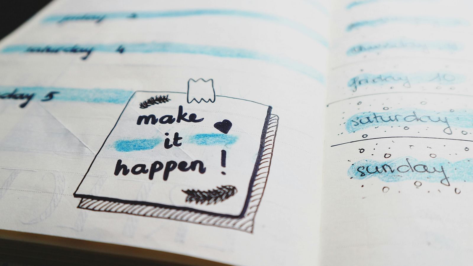 A notebook with the phrase Make It Happen written, alongside a marker pen.