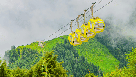 4 cable cars hang from wires above a lush green hillside shrouded in thick white mist.