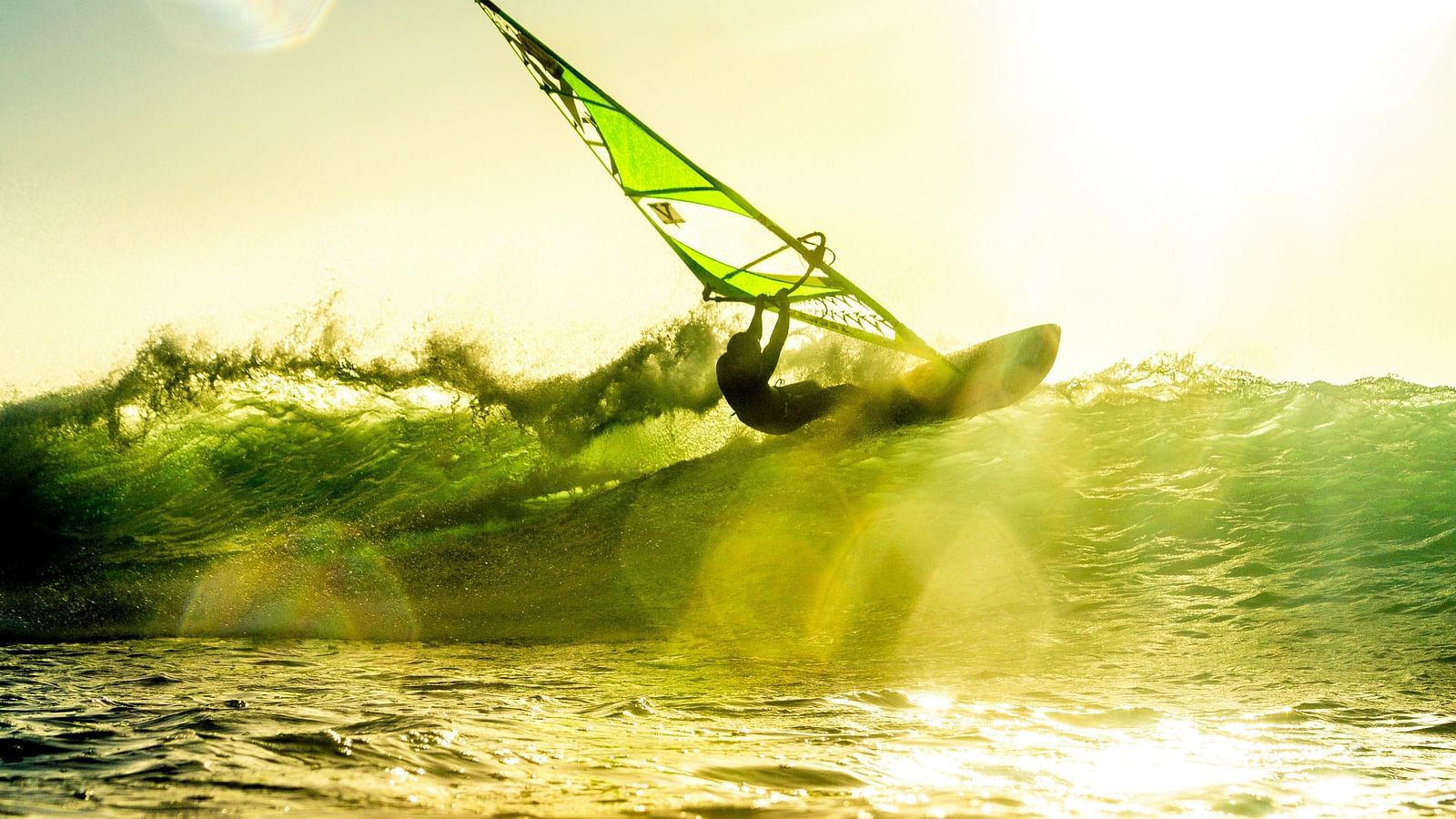 A person windsurfing on a wave with the sun shining down on the waterbody