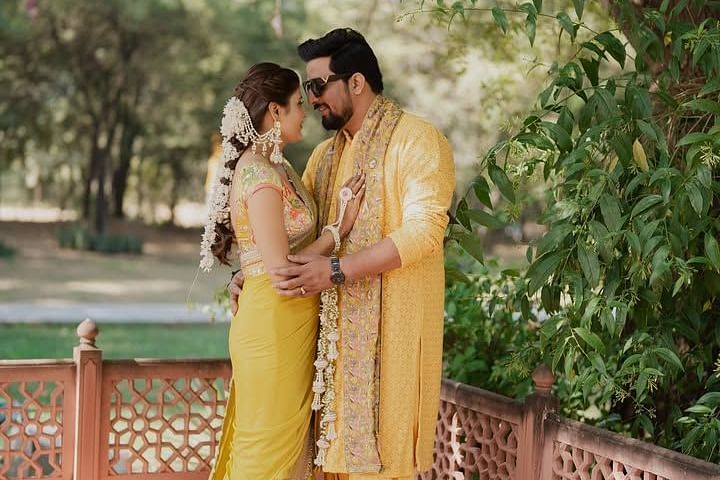 A couple in matching traditional attire shares an intimate moment in a lush garden, surrounded by greenery and soft light. - Umaid Palace - A Lakeside Heritage Palace Resort