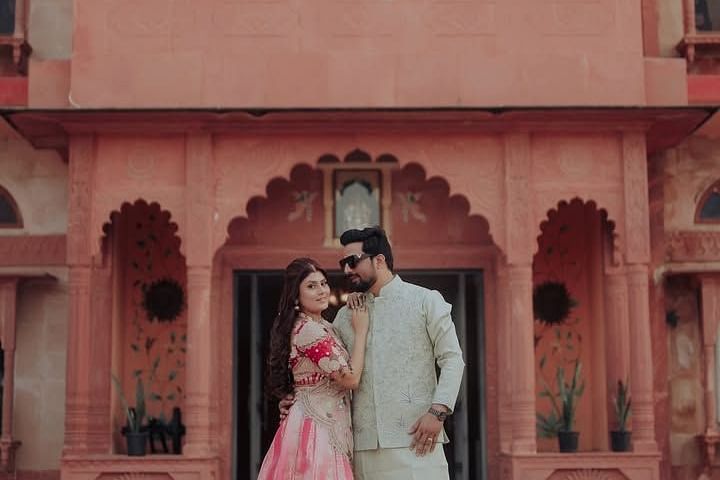 A couple poses elegantly in front of a grand heritage palace, with the bride in a wedding lehenga and the groom in a  sherwani. - Umaid Palace - A Lakeside Heritage Palace Resort