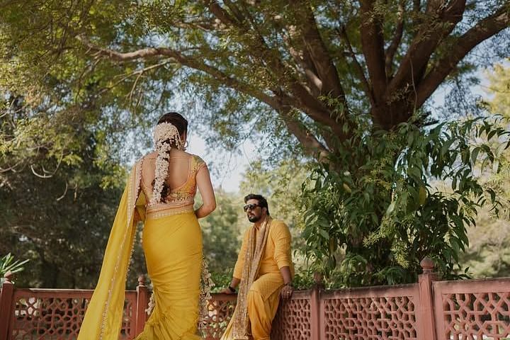 A woman walks gracefully towards a man sitting on a bench, surrounded by lush greenery and intricate architectural details. - Umaid Palace - A Lakeside Heritage Palace Resort