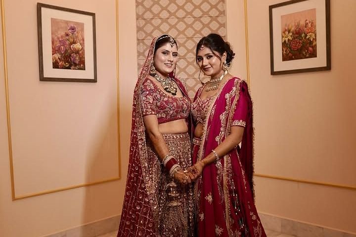Two women in elegant bridal attire stand hand in hand in a regal setting, adorned with intricate jewelry. Umaid Palace - A Lakeside Heritage Palace Resort