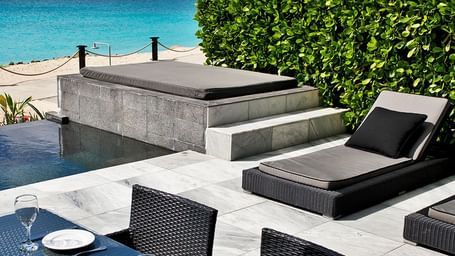 An outdoor patio with a dining table, lounge chairs, and a daybed overlooking the ocean and lush foliage at the Tamarind Hills Resort and Villas, Antigua.