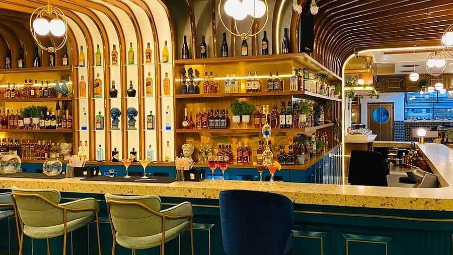 An image of a bar featuring a counter table, stools, and a shelf where liquor items are placed - Themis Barbecue House, Panipat