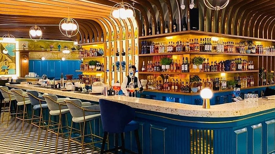 An image of a bar featuring a counter table, chairs, and a shelf where liquor items are placed - Themis Barbecue House, Panipat