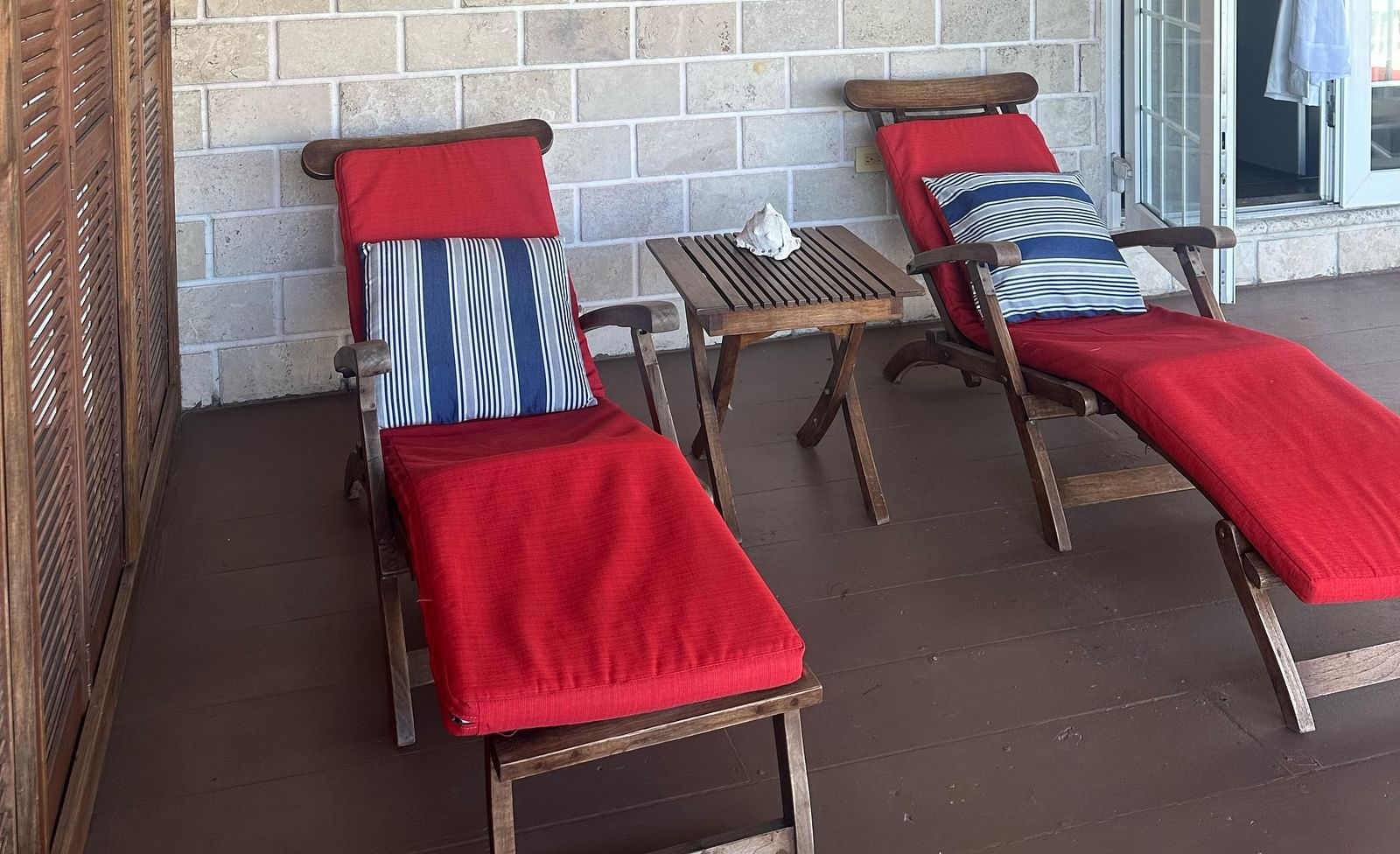 Covered porch with red lounge chairs and small tables outside a room | A Stone's Throw Away