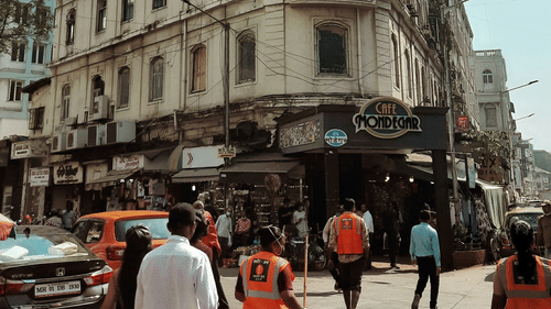 A tall building with curved architecture facing a busy street with people walking and vehicles passing.