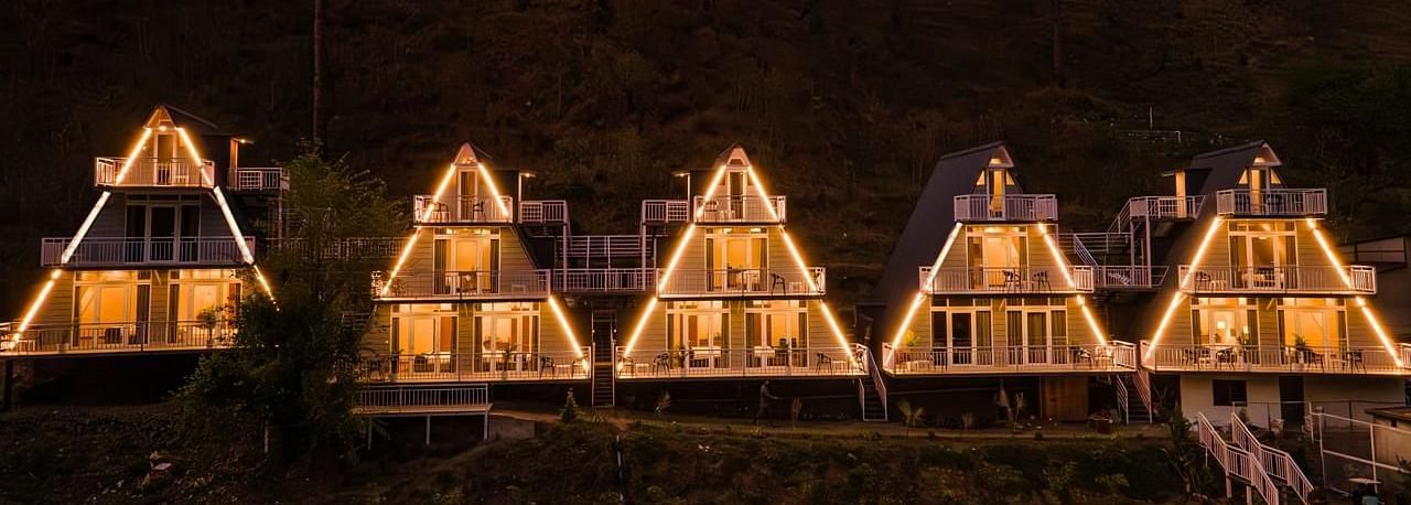 A nighttime view of four illuminated A-frame cottages, showcasing their distinctive architectural design.