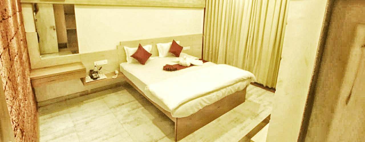 A spacious room with a large bed and windows beside it, covered with curtains. There is a wall-mounted mirror at SeaFort Beach Resort