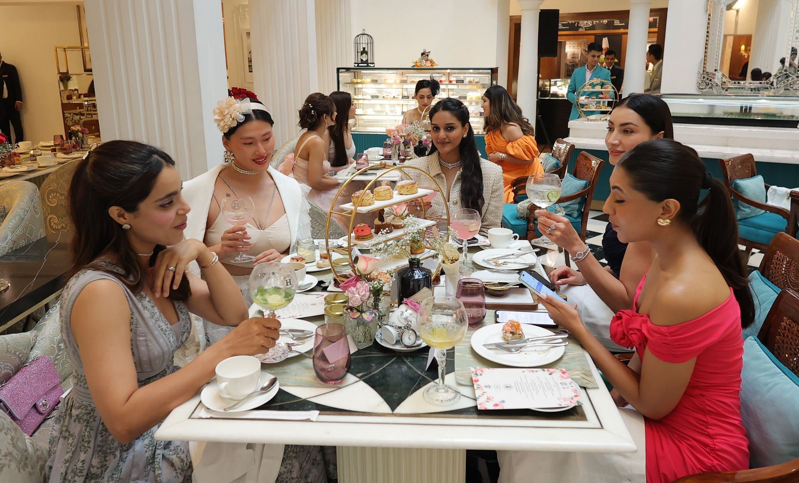 People enjoying their Buffet High Tea with an elegant setup featuring pastries and scones at The Claridges, New Delhi