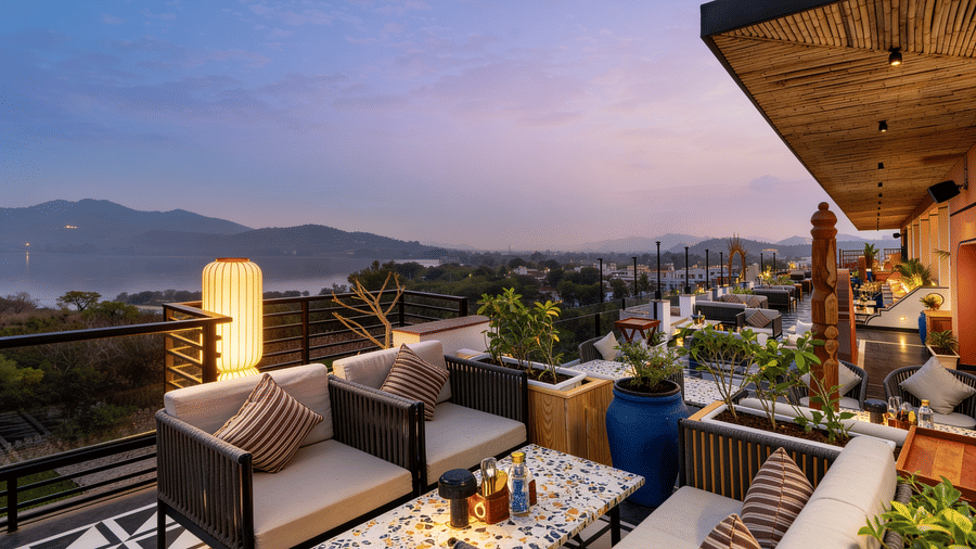 Armchairs and cushioned seating are arranged on a rooftop terrace at The Sierra - By The Lake, offering an open view of hills under an evening sky.