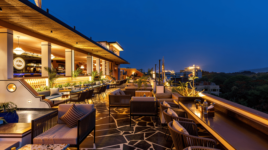Small dining tables and chairs are illuminated at night on the outdoor rooftop terrace of The Sierra - By The Lake, with distant city lights visible.
