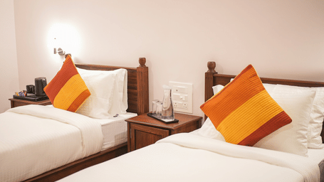 A bedroom featuring two single beds with white linens and orange and red gradient pillows | Daksh the Fateh Retreat