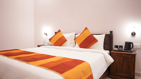 A bedroom featuring a double bed with a white duvet, an orange and red gradient runner and matching pillows | Daksh the Fateh Retreat