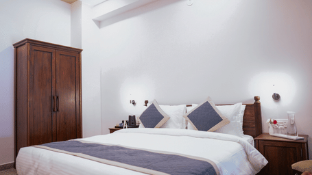 A bright bedroom with a double bed, white linens, blue cushions and a dark wooden wardrobe | Daksh the Fateh Retreat