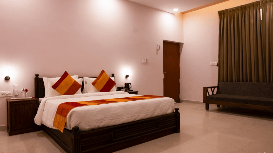 A spacious bedroom with a double bed, orange bedding accents and a wooden seating area | Daksh the Fateh Retreat