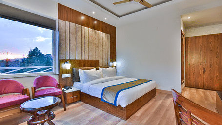 A large bed next to two cushioned chairs  in Premium Room With Balcony at DLS Ark Holiday Inn, Banikhet.