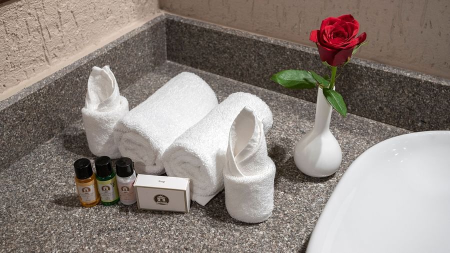Toiletries placed beside neatly folded towels and a small vase with a rose by the side for decoration - Stone Wood Nature Resort, Gokarna