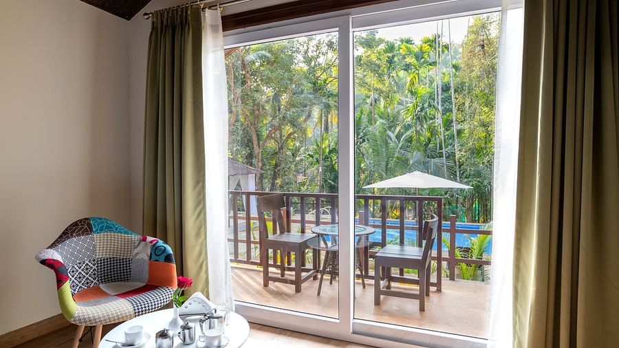 A hotel room with a colourful chair placed beside a sliding door opening to the balcony - Stone Wood Nature Resort, Gokarna