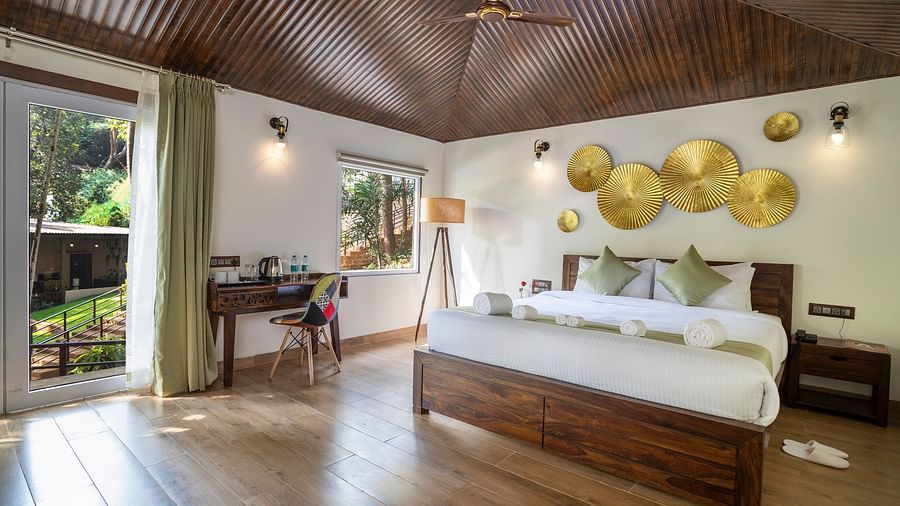 A hotel room with a large wooden bed and a door opening to the lush garden - Stone Wood Nature Resort, Gokarna