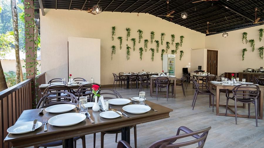 An open air restaurant with wooden tables and chairs, neatly arranged plates and cutlery and a wall with plants mounted on it - Stone Wood Nature Resort, Gokarna