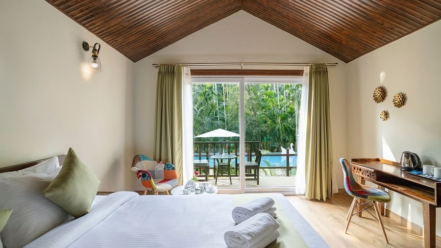 A view of a hotel room with comfortable bed, furniture and a balcony opening up to the pool - Stone Wood Nature Resort, Gokarna