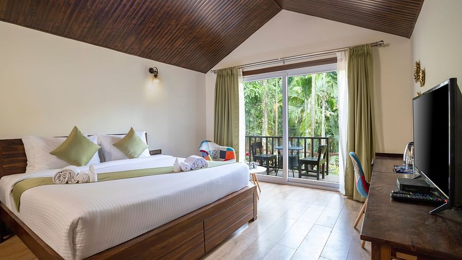 A hotel room with a garden view, a wall mounted television and a large bed - Stone Wood Nature Resort, Gokarna